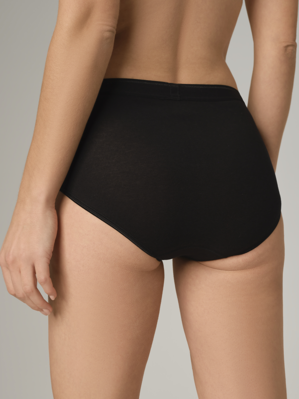 Rückansicht: Frau trägt Maxi-Slip von Comazo in der Farbe Schwarz Feinripp-Qualität