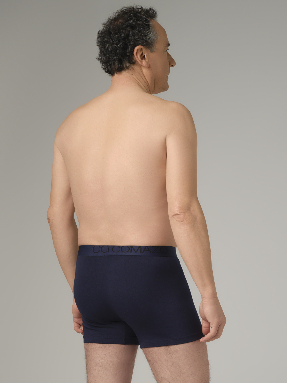 Rear view: Man wearing Comazo trunks in navy with logo waistband