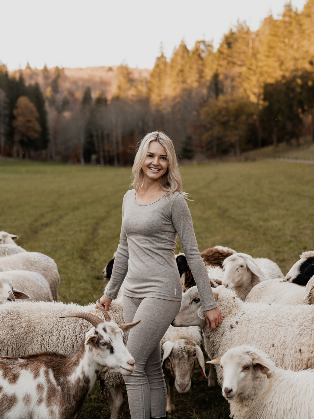 Frau trägt Merino-Funktionswäsche von Comazo und kniet zwischen Schafen – natürliche Wärme und Atmungsaktivität aus hochwertiger Merinowolle
