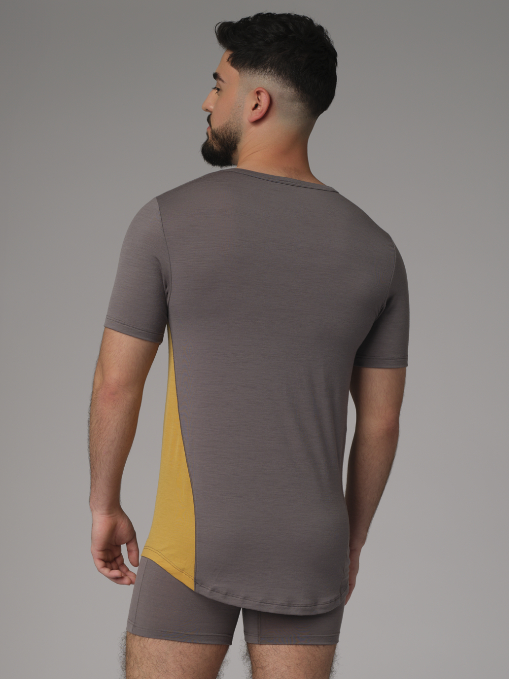 Rückansicht: Mann trägt Shirt kurzarm aus Merinowolle von Comazo in der Farbe Steelgrey/Senf mit längerem Rückenteil und Rundhalsausschnitt