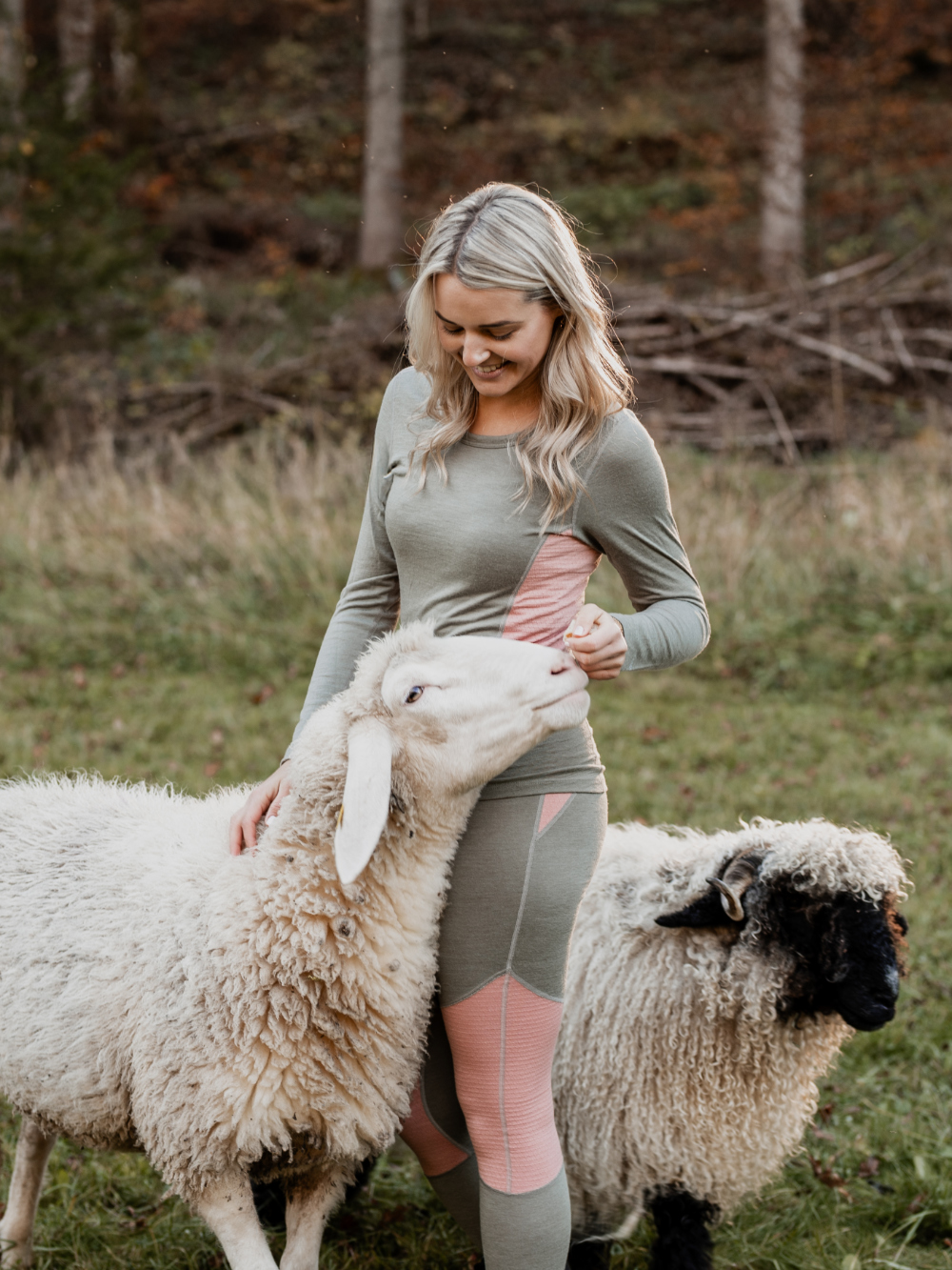 Frau in farbiger Merino-Funktionswäsche von Comazo kniet neben einem Schaf – natürliche Wärme und Komfort aus nachhaltiger Merinowolle.