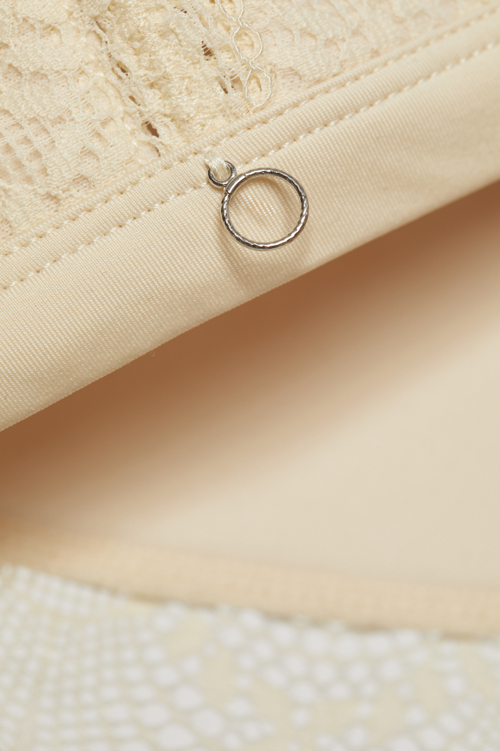 Detailbild Soft-BH von Comazo in der Farbe Cream mit zarter Spitze und rundem Accessoire-Anhänger.
