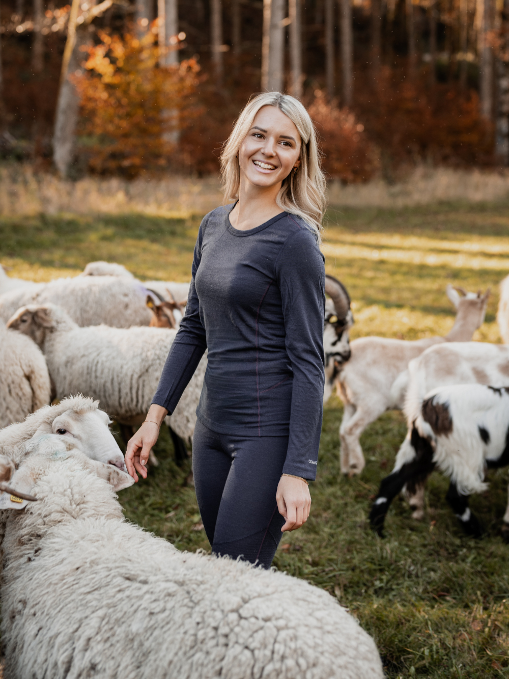 Vorderansicht in der Natur: Frau steht zwischen Schafen und trägt Merinowolle-Shirt langarm von Comazo in der Farbe Navy aus 100% mulesing-freier Schurwolle