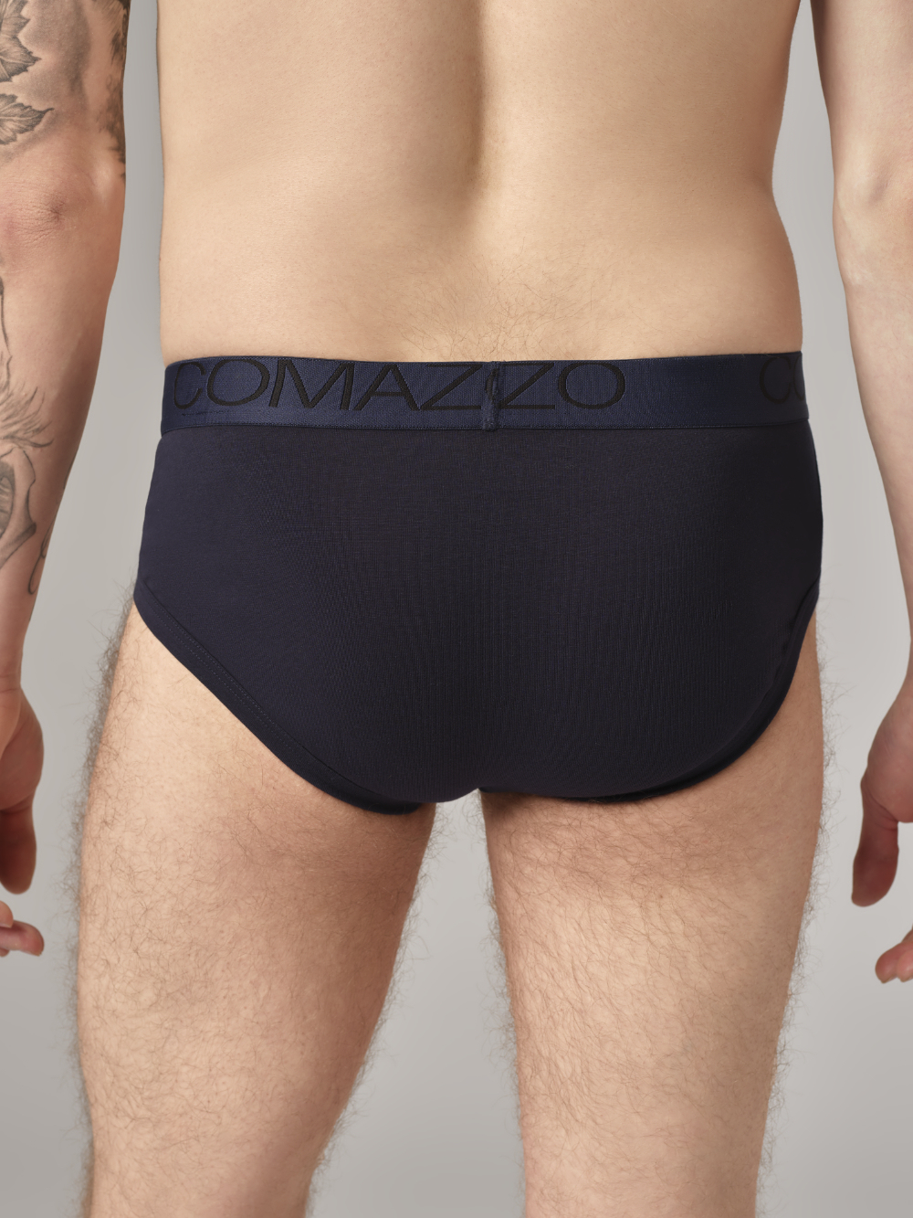 Rear view: Man wearing retro briefs by Comazo in navy with logo waistband