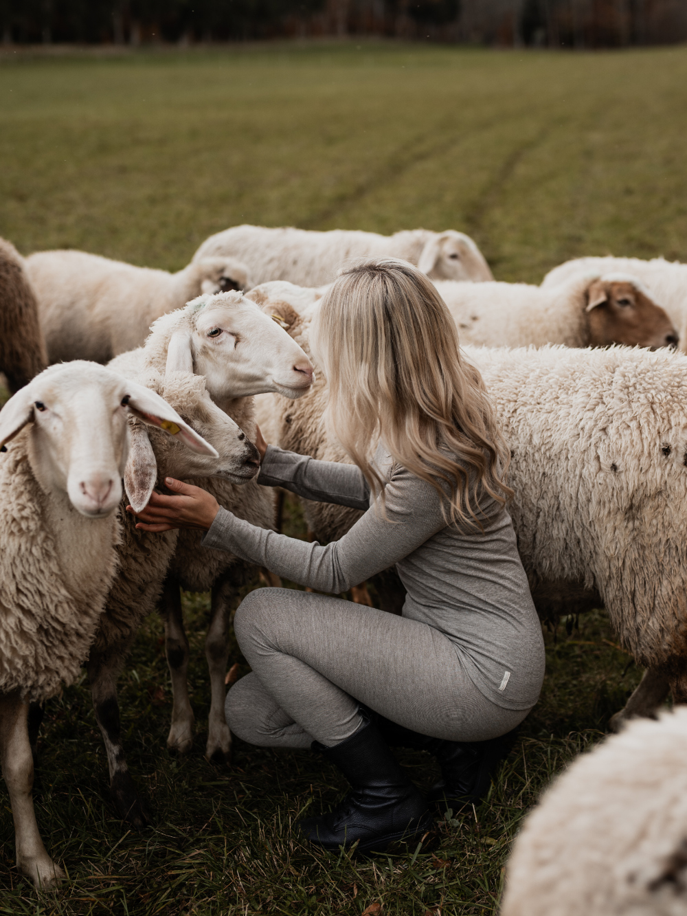 Frau trägt Merino-Funktionswäsche von Comazo und kniet zwischen Schafen – natürliche Wärme und Atmungsaktivität aus hochwertiger Merinowolle