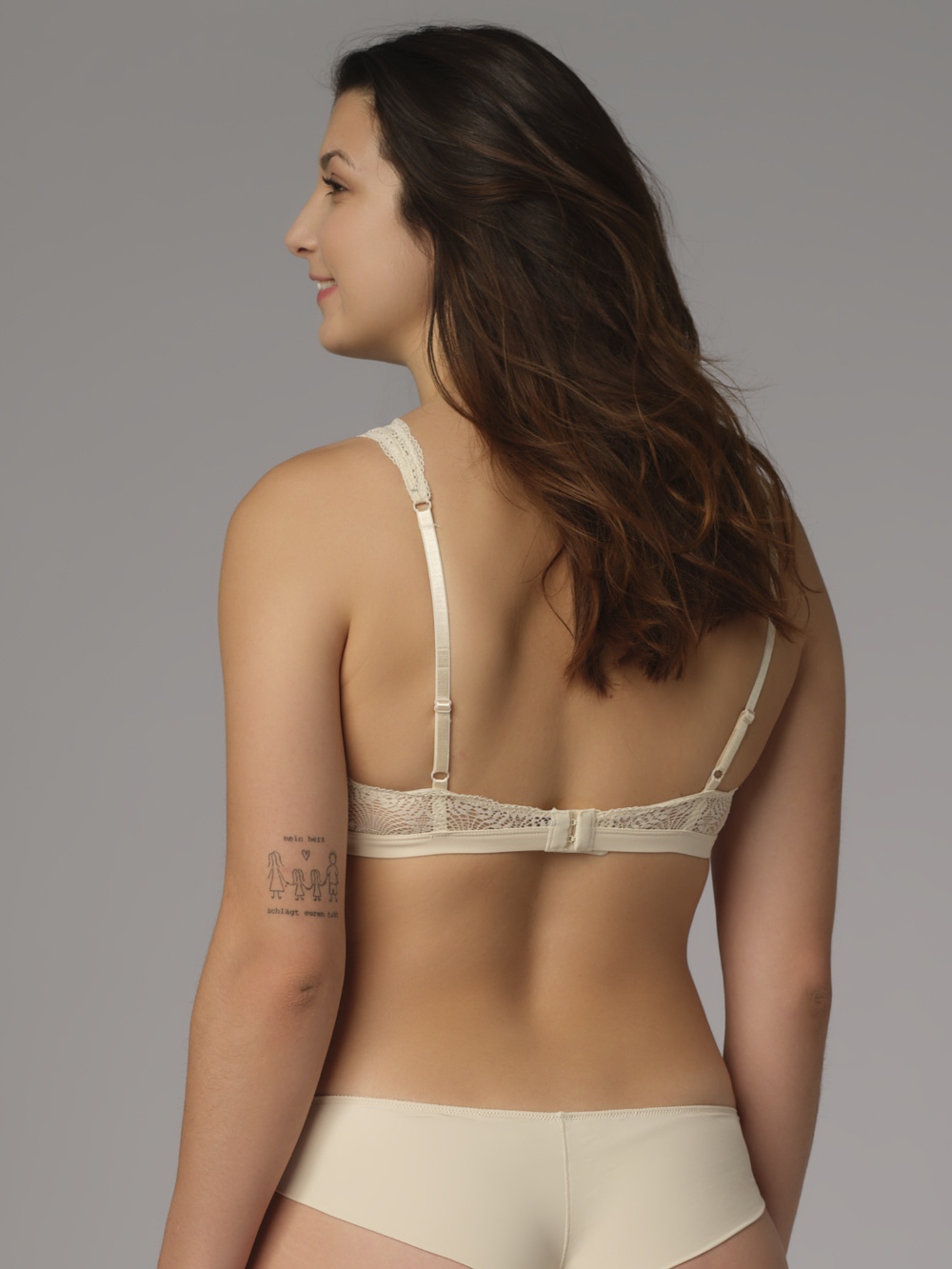 Rückansicht: Frau trägt Soft-BH von Comazo in der Farbe Cream mit zarter Spitze und rundem Accessoire-Anhänger.