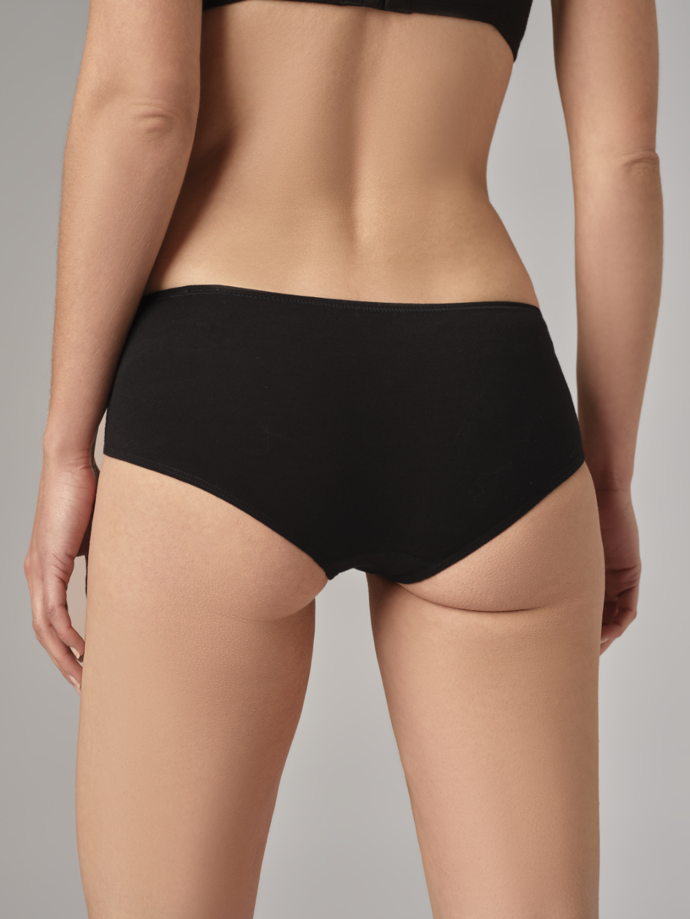 Rückansicht: Frau trägt Fairtrade Panty von Comazo in der Farbe Schwarz