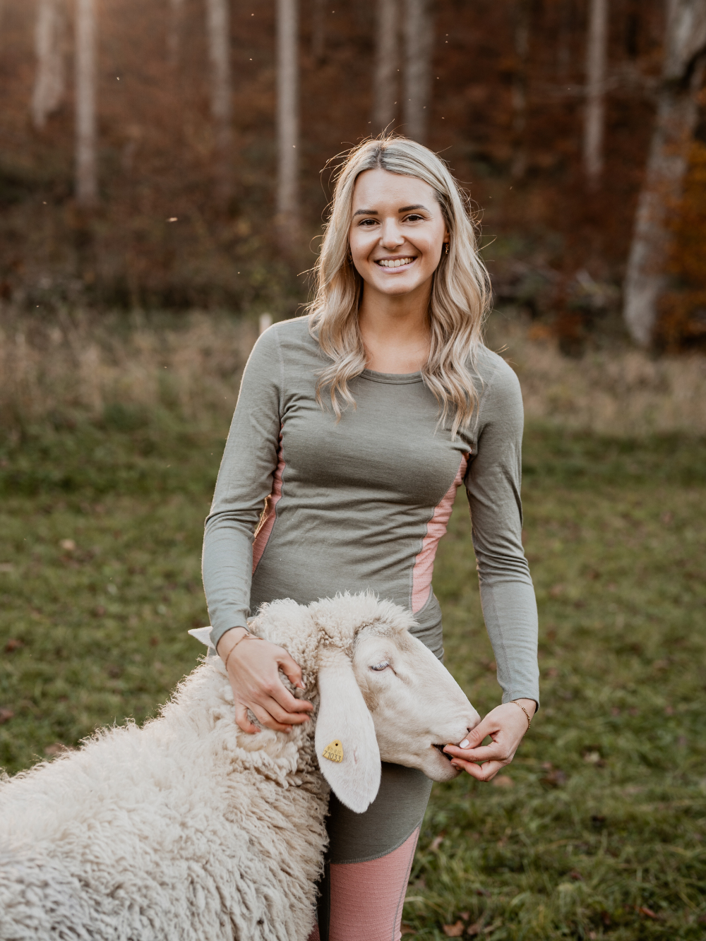 Frau trägt Merino-Funktionswäsche von Comazo und steht mit einem Schaf auf der Weide – natürliche Wärme und Atmungsaktivität aus hochwertiger Merinowolle.