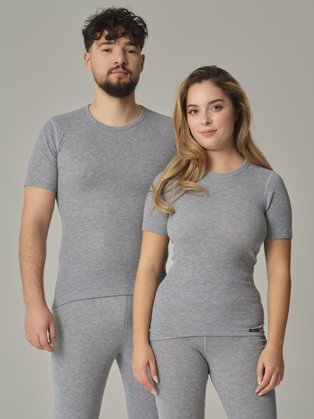 Vorderansicht: Eine Frau und ein Mann tragen Unisex Funktionsshirt "warm extra" kurzarm von Comazo in der Farbe Grau-Melange mit angerauter Innenseite zur optimalen Wärmespeicherung, Feuchtigkeitsmanagement und verlängertem Rückenteil