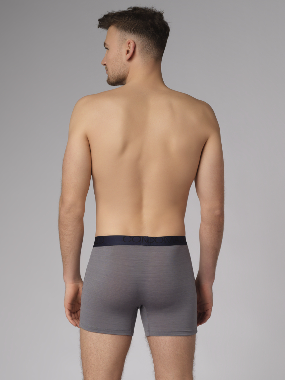 Rückansicht: Mann trägt Trunks aus Merinowolle von Comazo in der Farbe Grau/Navy mit Schriftzug am Bund