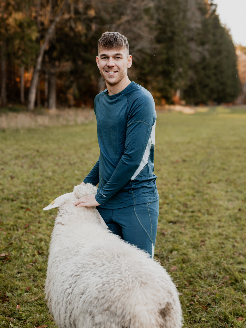 Mann trägt Merino-Funktionswäsche von Comazo und steht mit einem Schaf auf der Weide – natürliche Wärme und Atmungsaktivität aus Merinowolle