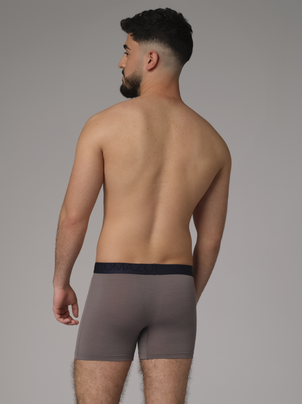 Rückansicht: Mann trägt Trunks aus Merinowolle von Comazo in der Farbe Steelgrey/Senf mit Schriftzug am Bund