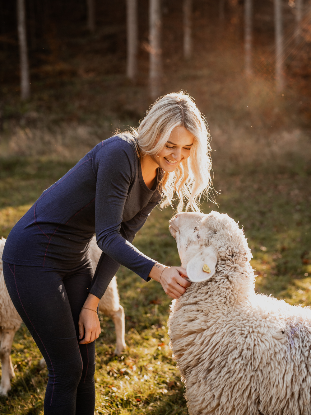 Vorderansicht in der Natur: Frau streichelt Schaf und trägt Merinowolle-Shirt langarm von Comazo in der Farbe Navy aus 100% mulesing-freier Schurwolle